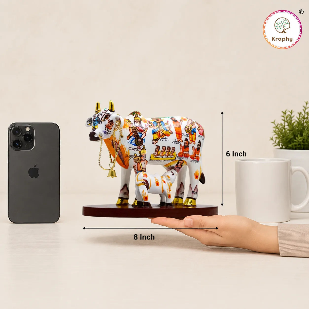 Decorative cow figurine with smartphone for scale, held by a hand, on a neutral background.